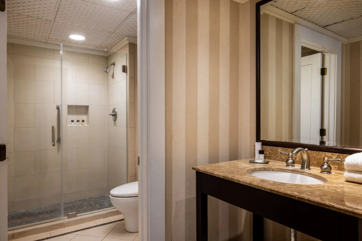 A serene, well-appointed bathroom with a glass-enclosed shower area, a modern vanity, and a large mirror. The clean lines and soft lighting evoke a spa-like sense of calm and relaxation, adding a layer of luxury to the guest suite experience.