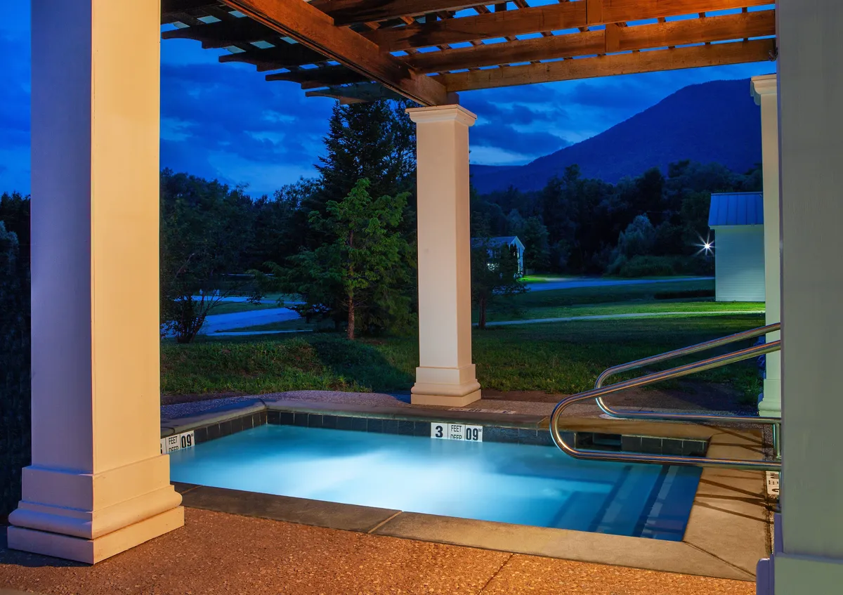 An inviting swimming pool framed by a wooden pergola and lush greenery, with a backdrop of rolling mountains. The serene setting evokes relaxation and offers a taste of the resort’s recreational amenities, including swimming and peaceful gathering spots.