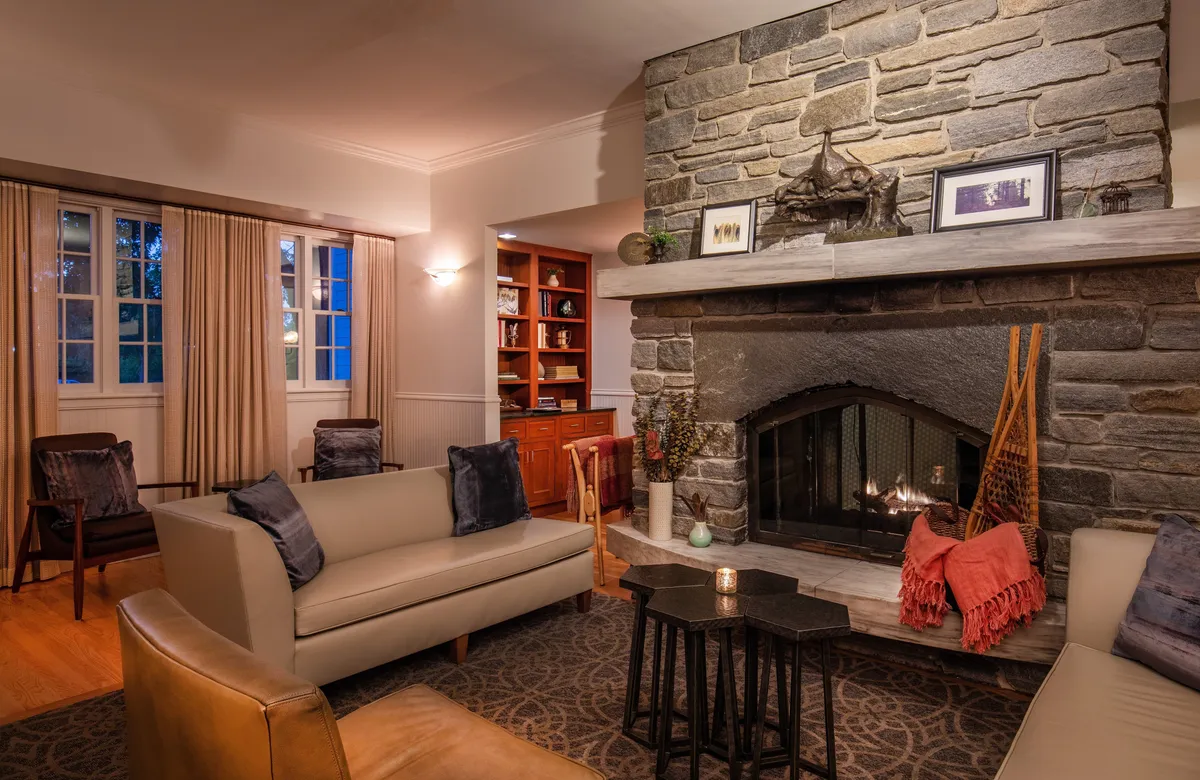 A warm, tastefully decorated interior centered on a stone fireplace surrounded by comfortable seating and wooden accents. Decorative accessories and plush chairs create a cozy spot for relaxation, reading, or spending quality time with loved ones, capturing the essence of a luxurious retreat.