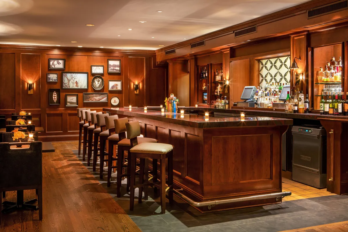 This image captures the inviting bar area of Equinox Resort, featuring comfortable stools, elegant framed artwork, and a well-stocked bar. The scene hints at the lively social atmosphere and sophisticated gatherings that occur here, complementing the resort's historic charm and hospitality.